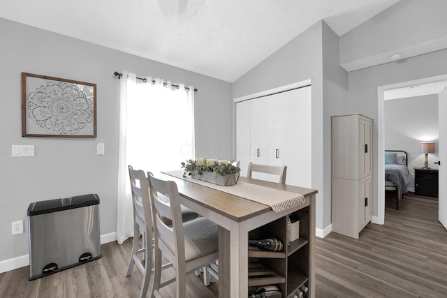 dining area featuring lofted ceiling, a textured ceiling, baseboards, and wood finished floors