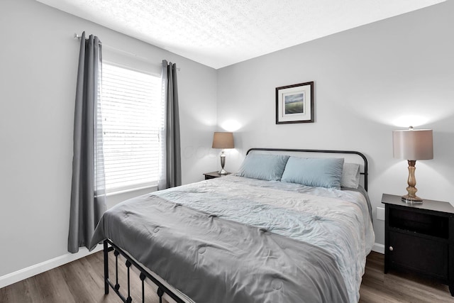 bedroom with a textured ceiling, baseboards, and wood finished floors