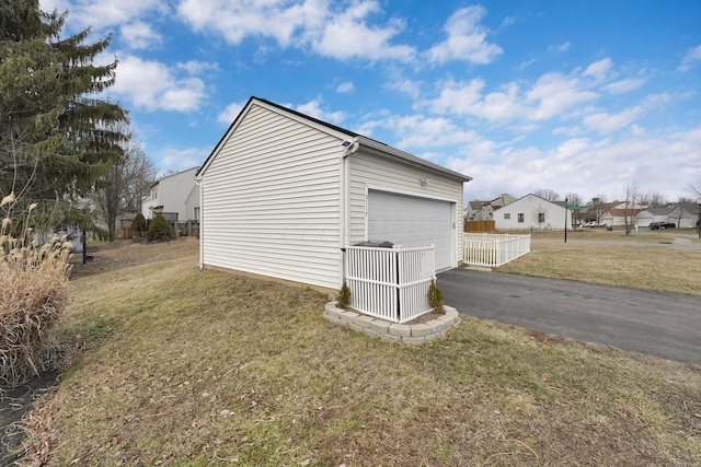 view of property exterior with a detached garage, fence, and a lawn