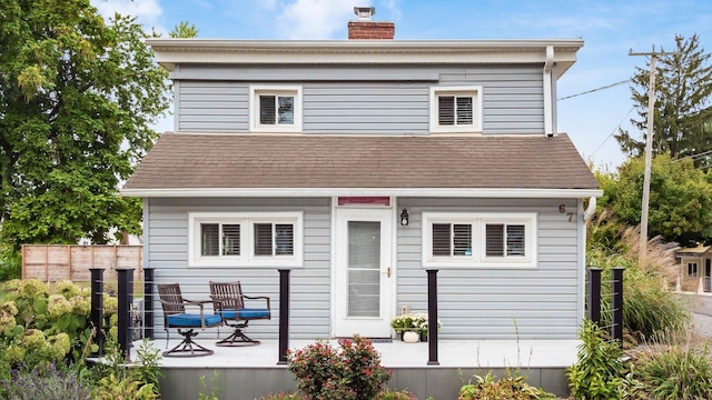 back of property with covered porch, a shingled roof, a chimney, and fence