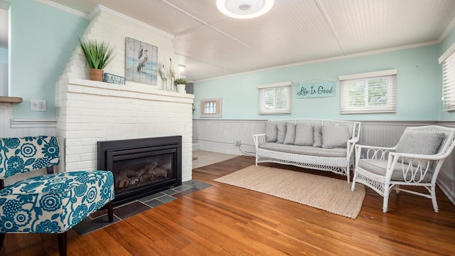 living room with a large fireplace, a wainscoted wall, crown molding, and wood finished floors