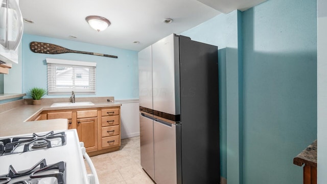 kitchen with light countertops, white gas range oven, a sink, and freestanding refrigerator