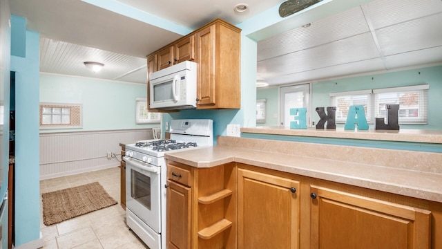 kitchen featuring a wainscoted wall, light tile patterned floors, light countertops, brown cabinetry, and white appliances