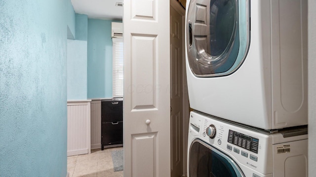 laundry room featuring light tile patterned floors, visible vents, wainscoting, stacked washing maching and dryer, and laundry area