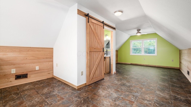 additional living space with lofted ceiling, a barn door, wooden walls, baseboards, and stone finish floor