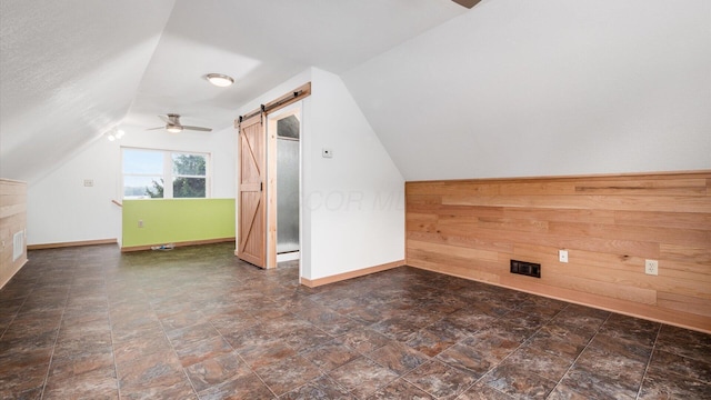 bonus room featuring lofted ceiling, visible vents, a barn door, wood walls, and baseboards