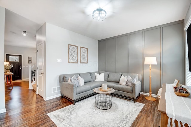 living area with baseboards, visible vents, dark wood-type flooring, stairs, and a decorative wall