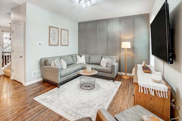 living area featuring visible vents, a decorative wall, wood finished floors, baseboards, and stairs