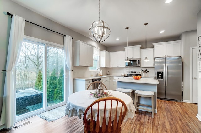 kitchen with visible vents, wood finished floors, a center island, stainless steel appliances, and light countertops