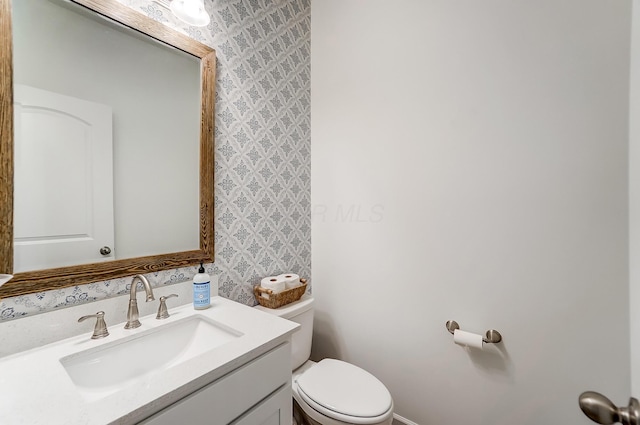 bathroom featuring toilet, wallpapered walls, and vanity