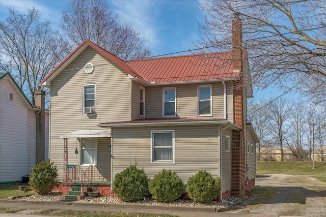 traditional-style home featuring a chimney, a standing seam roof, and metal roof