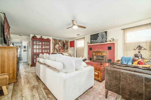 living room with a ceiling fan, a brick fireplace, a healthy amount of sunlight, and light wood-type flooring