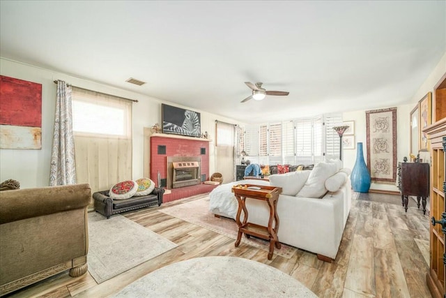 living area featuring wood finished floors, a fireplace, visible vents, and ceiling fan