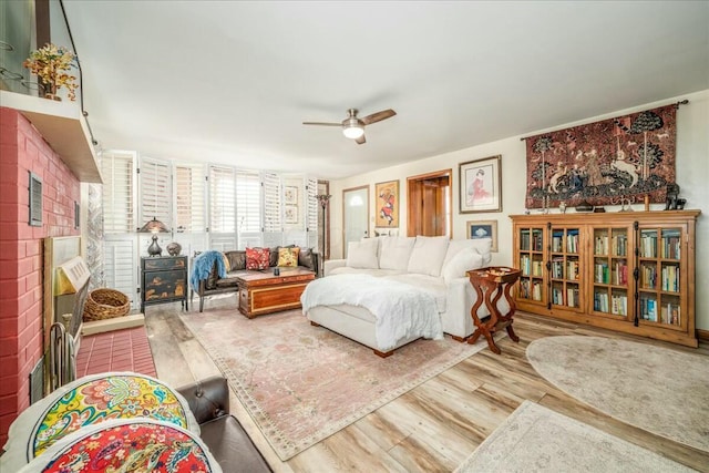 living area featuring a fireplace, a ceiling fan, and wood finished floors