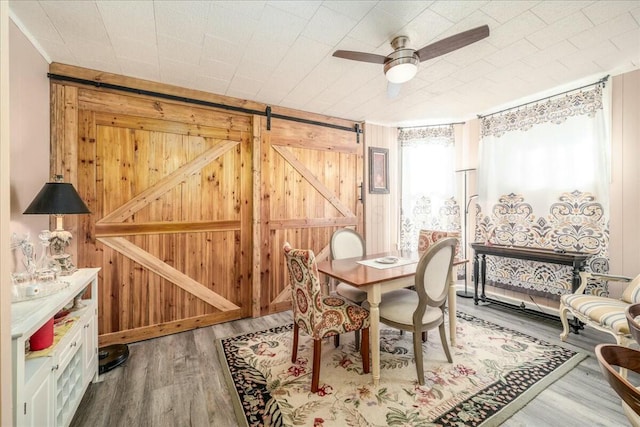 dining room with wooden walls, ceiling fan, a barn door, and wood finished floors