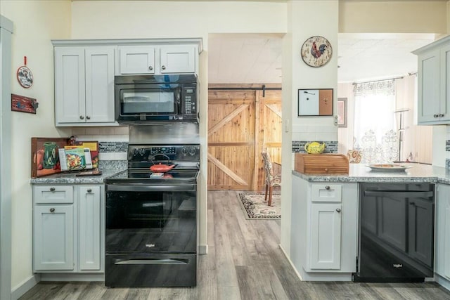 kitchen featuring wood finished floors, baseboards, black appliances, a barn door, and backsplash