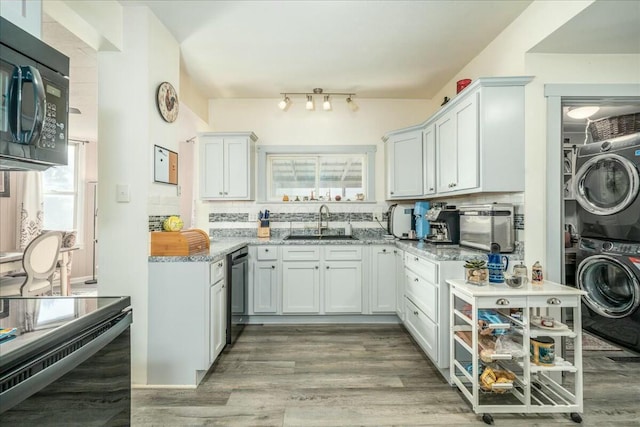 kitchen with light stone counters, a sink, black appliances, stacked washer and dryer, and tasteful backsplash