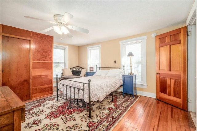 bedroom with multiple windows, a ceiling fan, baseboards, and light wood finished floors