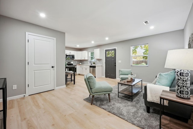 living room featuring baseboards, light wood-type flooring, visible vents, and recessed lighting