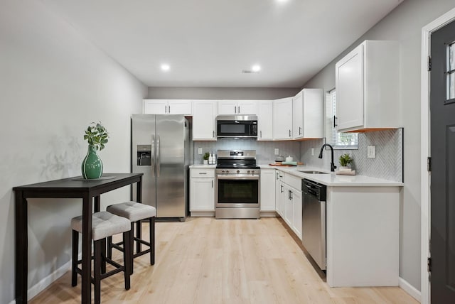 kitchen featuring light wood-style flooring, stainless steel appliances, a sink, light countertops, and tasteful backsplash