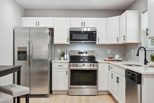 kitchen featuring white cabinets, a sink, stainless steel appliances, light countertops, and backsplash