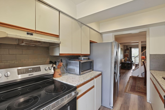 kitchen featuring backsplash, under cabinet range hood, light wood-style flooring, appliances with stainless steel finishes, and cream cabinetry