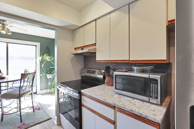 kitchen with light wood-type flooring, under cabinet range hood, tasteful backsplash, appliances with stainless steel finishes, and ceiling fan