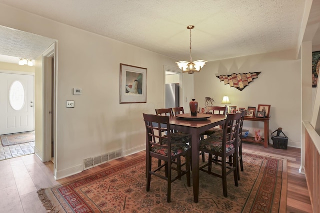 dining space with wood finished floors, baseboards, visible vents, a textured ceiling, and a notable chandelier