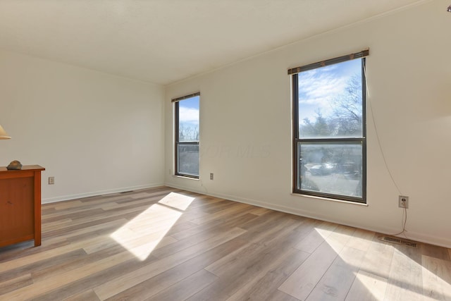 empty room featuring light wood-style floors, visible vents, and baseboards