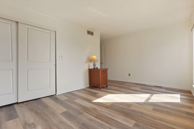 unfurnished bedroom with light wood-style flooring, baseboards, visible vents, and a closet