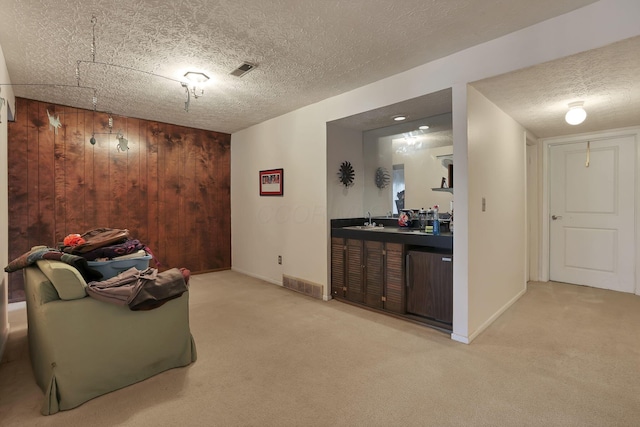 sitting room with visible vents, wood walls, indoor wet bar, carpet flooring, and a textured ceiling