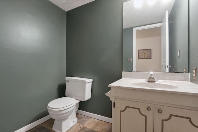 half bathroom featuring toilet, a textured ceiling, vanity, and baseboards