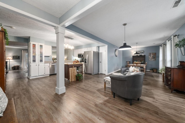 living room with dark wood-style flooring, visible vents, a textured ceiling, and ornate columns