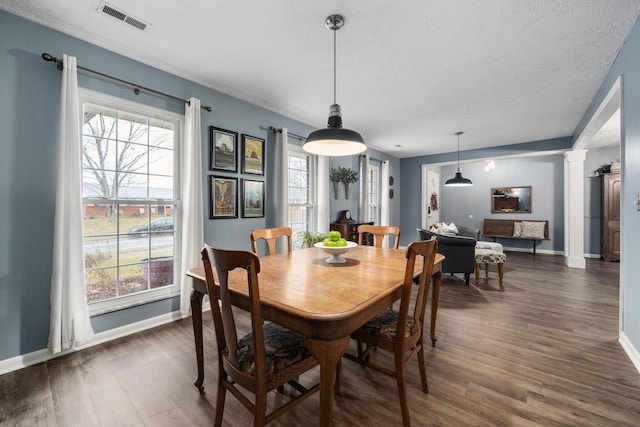 dining room featuring decorative columns, visible vents, dark wood-type flooring, a textured ceiling, and baseboards