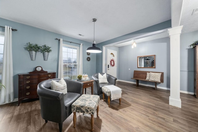 living area featuring decorative columns, visible vents, baseboards, and wood finished floors