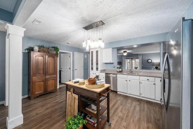 kitchen with appliances with stainless steel finishes, dark wood-type flooring, a sink, and decorative columns