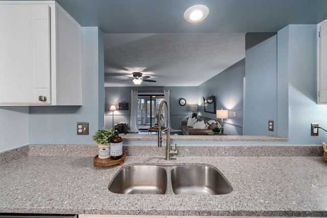 kitchen with a textured ceiling, a sink, a ceiling fan, white cabinets, and open floor plan