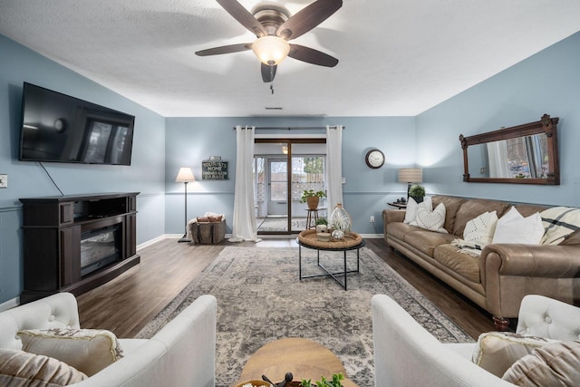 living area featuring a glass covered fireplace, wood finished floors, a ceiling fan, and baseboards