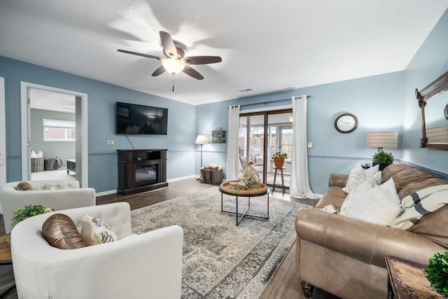 living area featuring ceiling fan, wood finished floors, plenty of natural light, and a glass covered fireplace