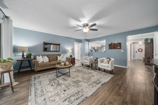 living room featuring a textured ceiling, ceiling fan, wood finished floors, and baseboards