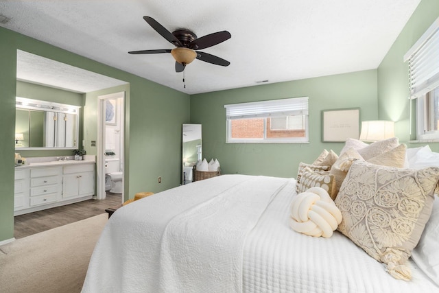 bedroom with visible vents, a ceiling fan, ensuite bath, wood finished floors, and a sink