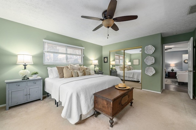 bedroom with a closet, visible vents, light carpet, a textured ceiling, and baseboards