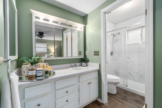 full bath with a stall shower, a ceiling fan, toilet, wood finished floors, and vanity