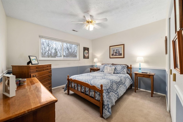 bedroom featuring light colored carpet, visible vents, a ceiling fan, a textured ceiling, and baseboards