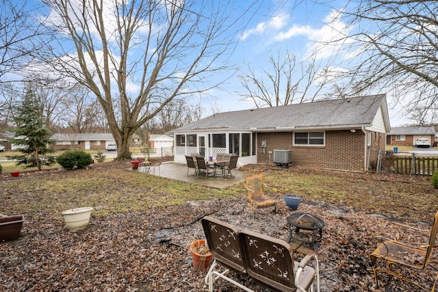 back of house featuring an outdoor fire pit, central AC unit, a sunroom, fence, and brick siding