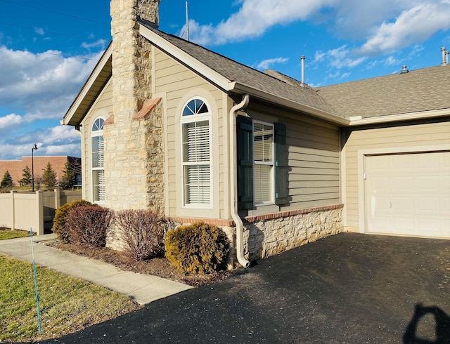 view of home's exterior with a garage, a shingled roof, fence, driveway, and a chimney