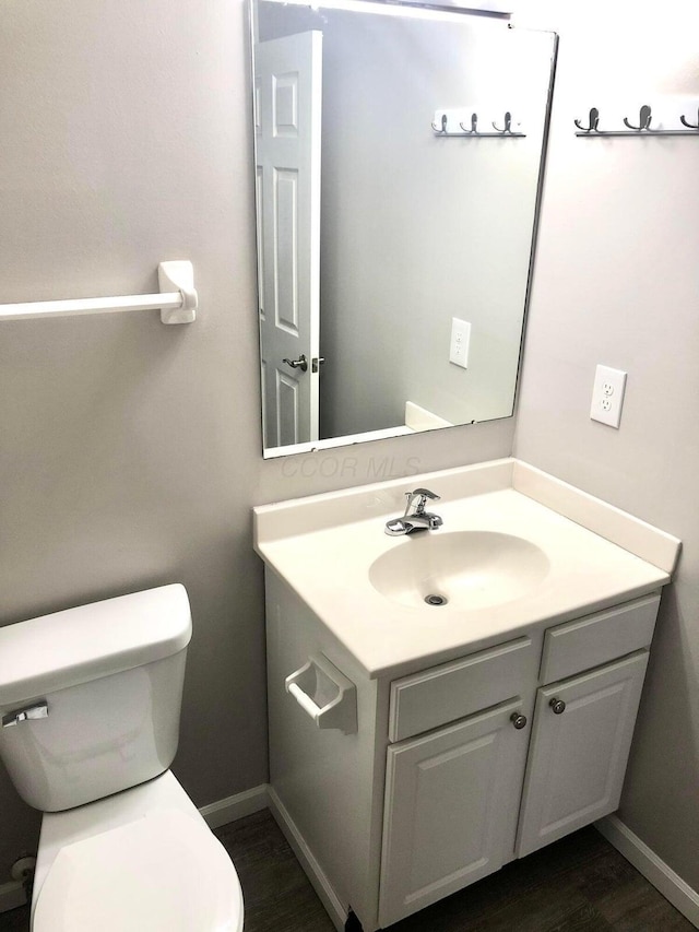 bathroom featuring baseboards, toilet, wood finished floors, and vanity