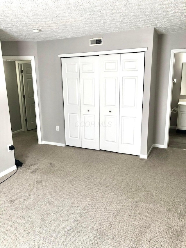 unfurnished bedroom featuring visible vents, baseboards, carpet, a closet, and a textured ceiling