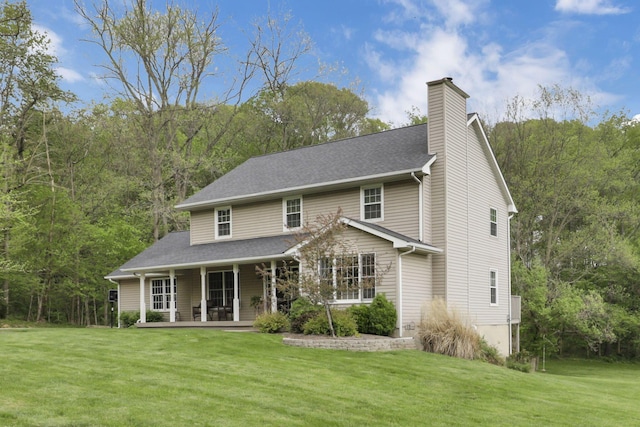 back of house featuring a wooded view, a yard, covered porch, and a chimney