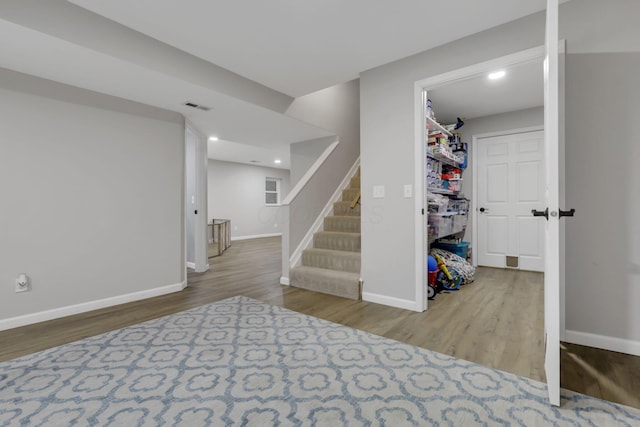 finished below grade area featuring stairway, baseboards, wood finished floors, and visible vents
